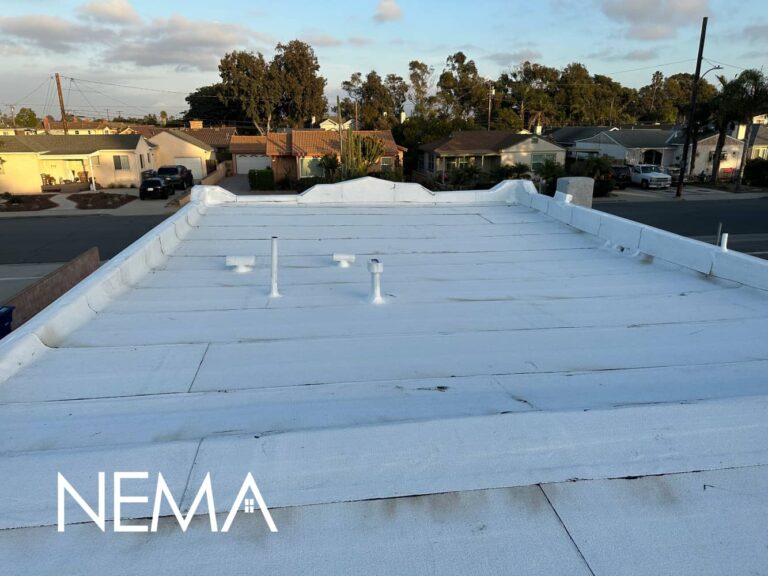 White flat roof with roof vents, homes and trees behind