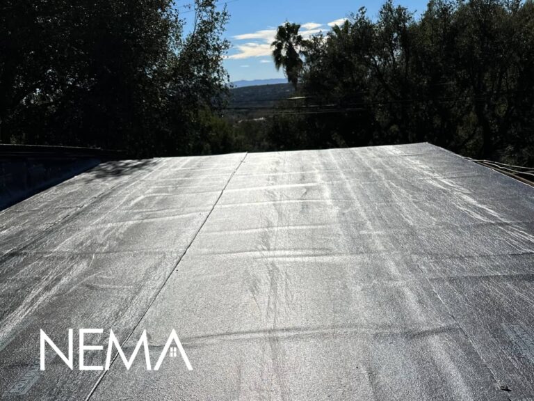 Flat roof with smooth gray roll roofing, trees around the house