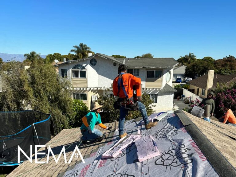 Roofers working on a roof covered with underlayment, houses and palm trees behind