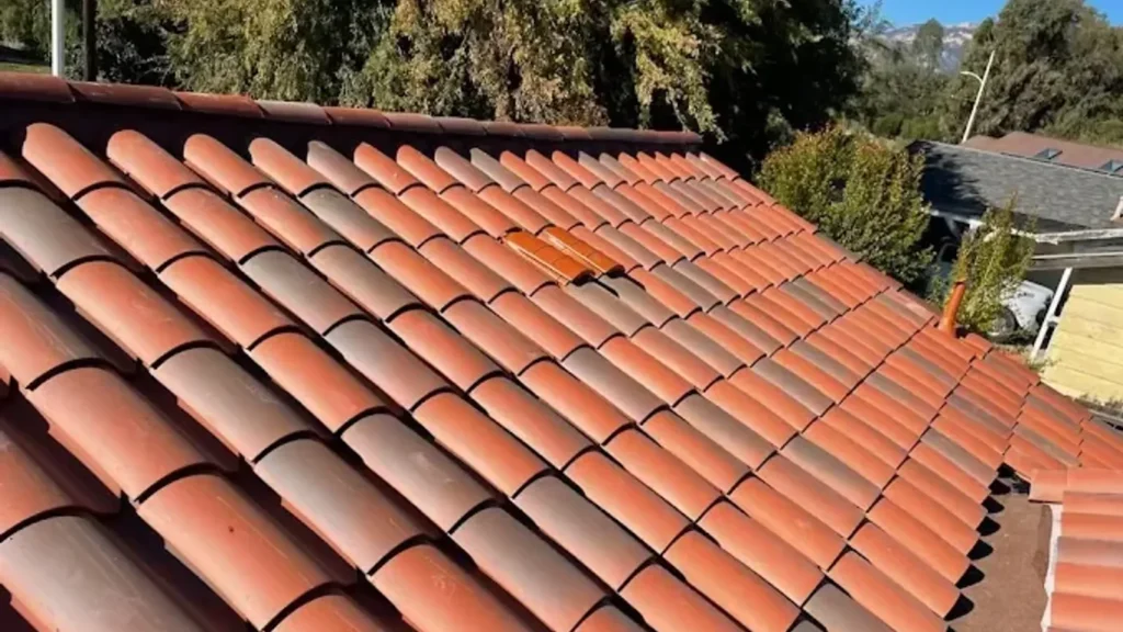A roofing professional in work boots carefully lifting a weathered clay mission tile on a sun-bleached Spanish Colonial
