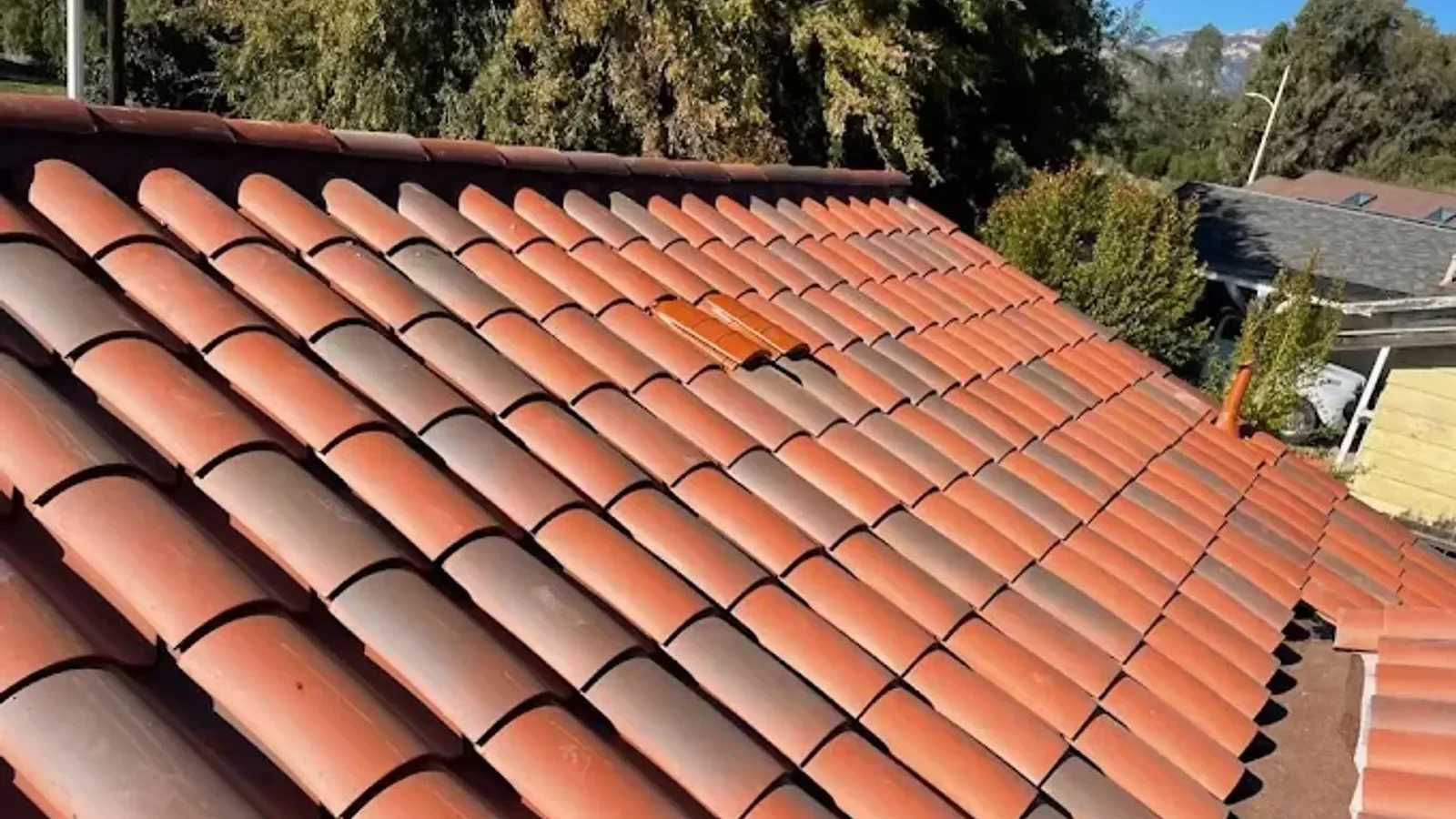 A roofing professional in work boots carefully lifting a weathered clay mission tile on a sun-bleached Spanish Colonial