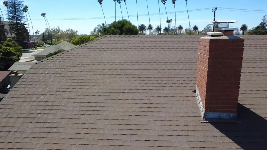 Shingle roof with a brick chimney and palm trees beyond, roofed by NEMA Roofing
