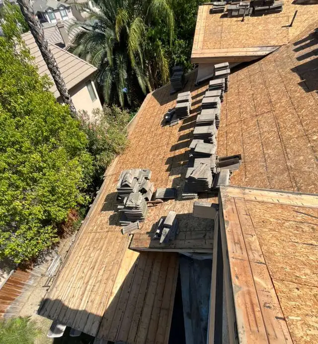 Concrete roof tiles stacked on a new wood deck beside a section of old board deck during a tile roof re-deck in Corona